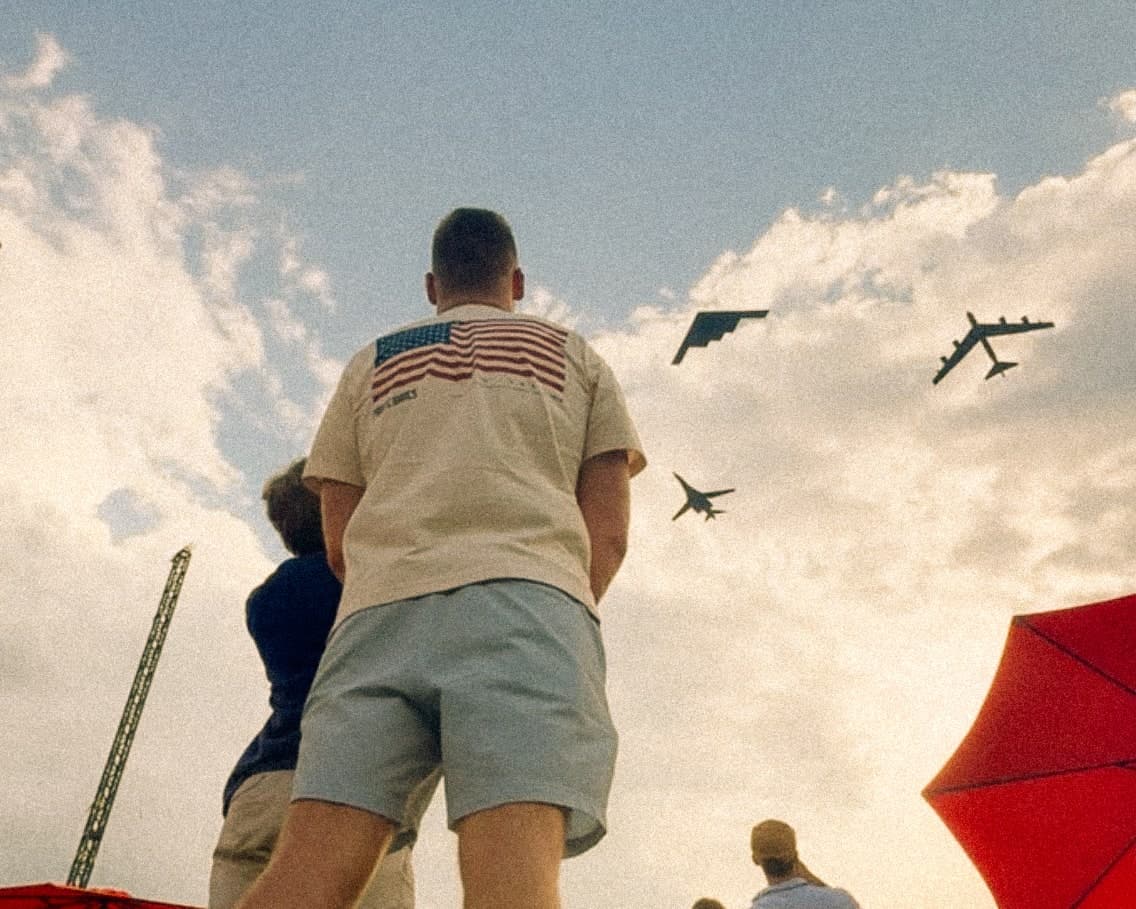 Matthew Tortora, in an American-flag shirt, watching a military flyover at an airshow